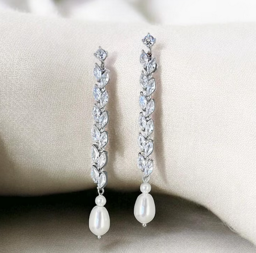 Pair of silver earrings with clear gemstones and pearl drops on a beige surface