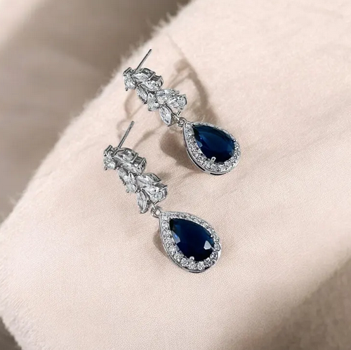 Close-up of sapphire teardrop earrings highlighting crystal halo setting and deep blue color