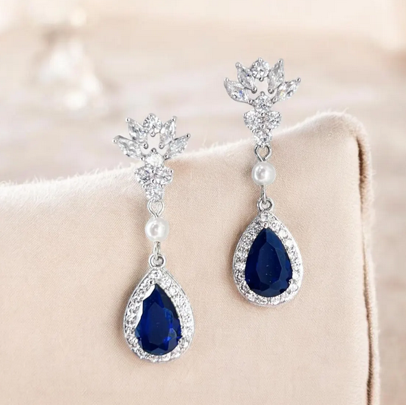 Pair of blue teardrop earrings with silver and pearl accents on a beige surface.