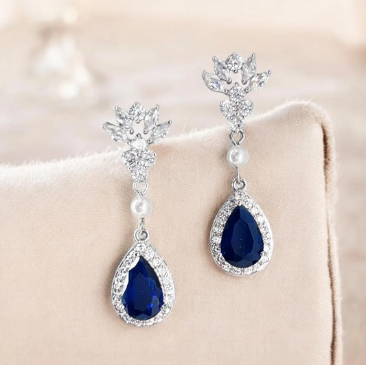 Pair of blue teardrop earrings with silver and pearl accents on a beige surface.