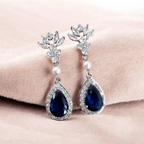 Pair of earrings with blue teardrop stones and pearl accents on a pink fabric background