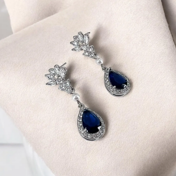 Pair of blue teardrop earrings with silver accents on a light pink surface