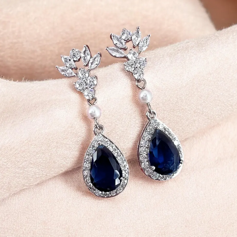 Pair of blue teardrop earrings with floral tops held against a light skin background