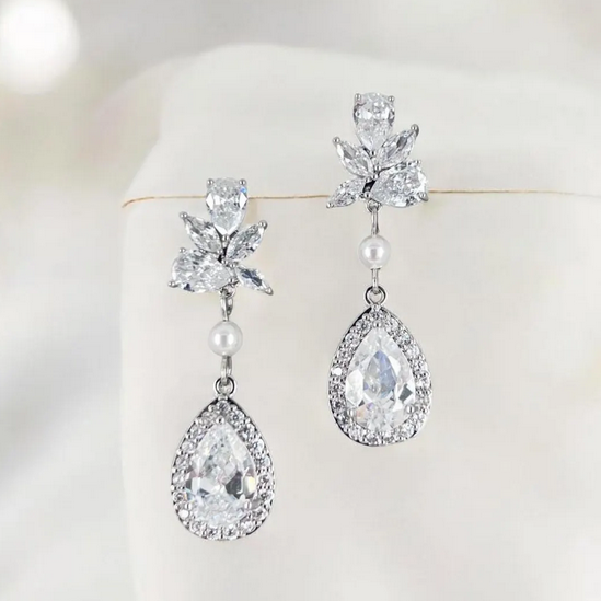 Pair of silver earrings with clear gemstones and pearls on a white background