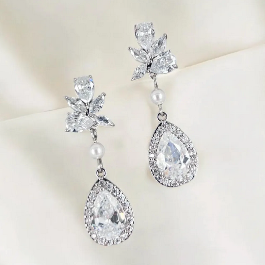 Pair of silver teardrop earrings with clear gemstones and pearls on a light background