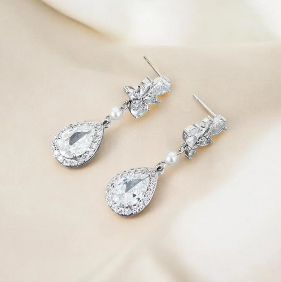 Pair of silver teardrop earrings with clear gemstones and pearls on a beige background