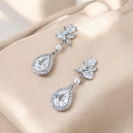 Pair of silver teardrop earrings with floral tops on a beige background