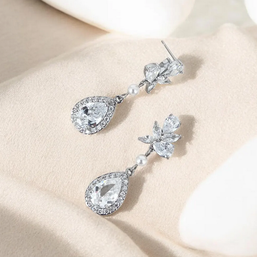 Silver teardrop earrings with clear gemstones and pearls on a beige surface