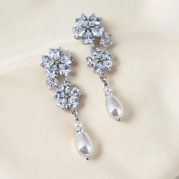 Pair of silver earrings with floral designs and pearl-like drops on a beige background