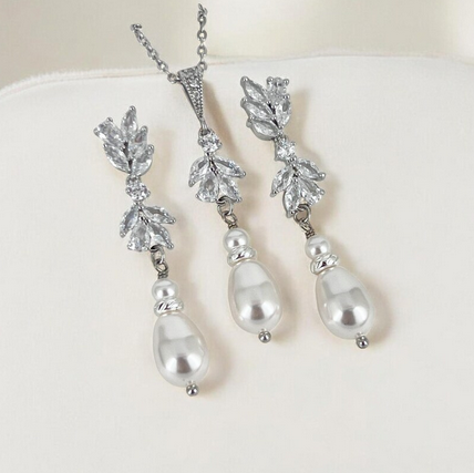 Silver earrings and necklace with pearl drops on a white cushion
