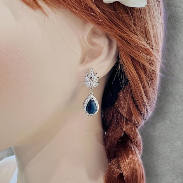 Close-up of a person wearing a sparkling sapphire blue teardrop bridal clip earrings