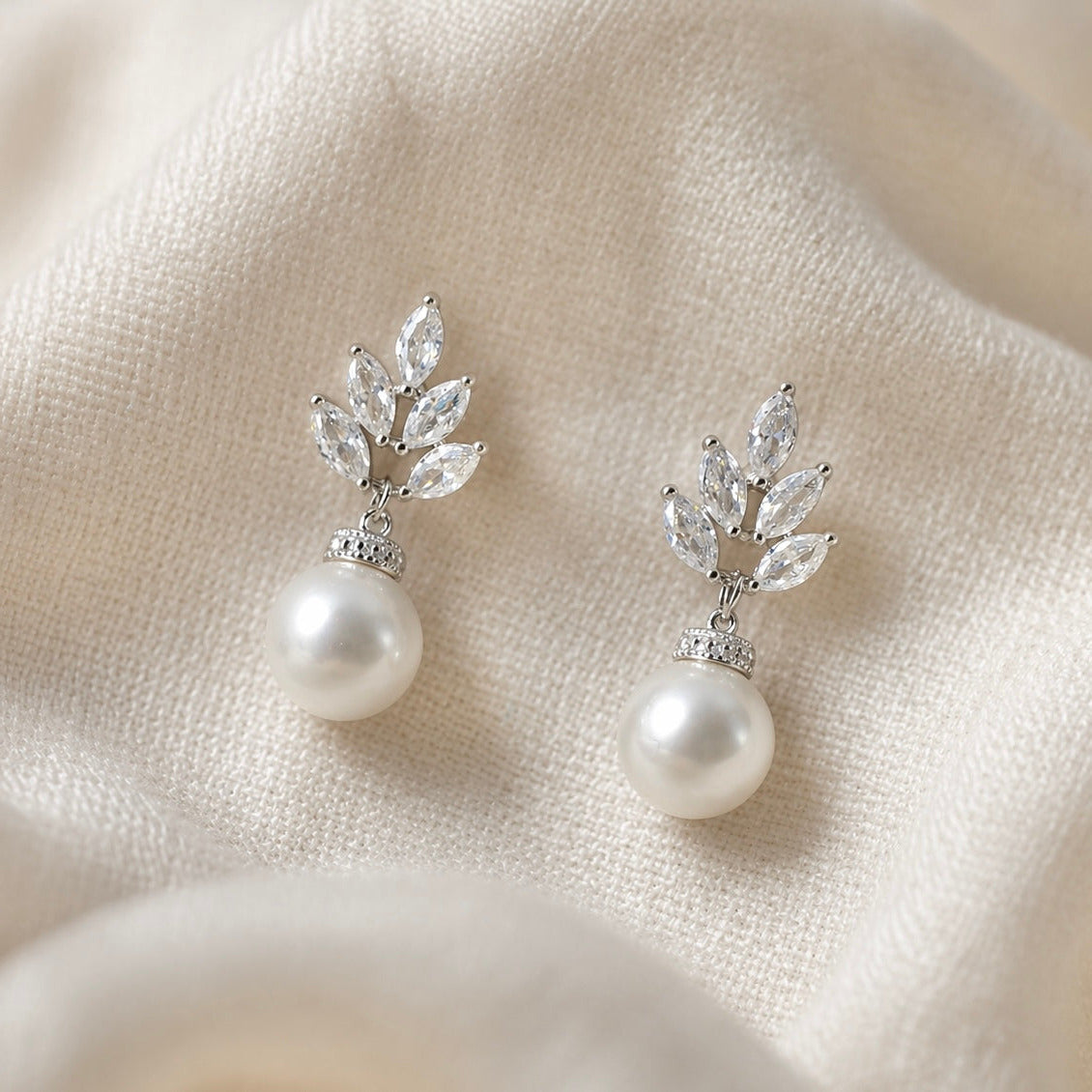 Pearl earrings with leaf-like designs on a beige fabric background