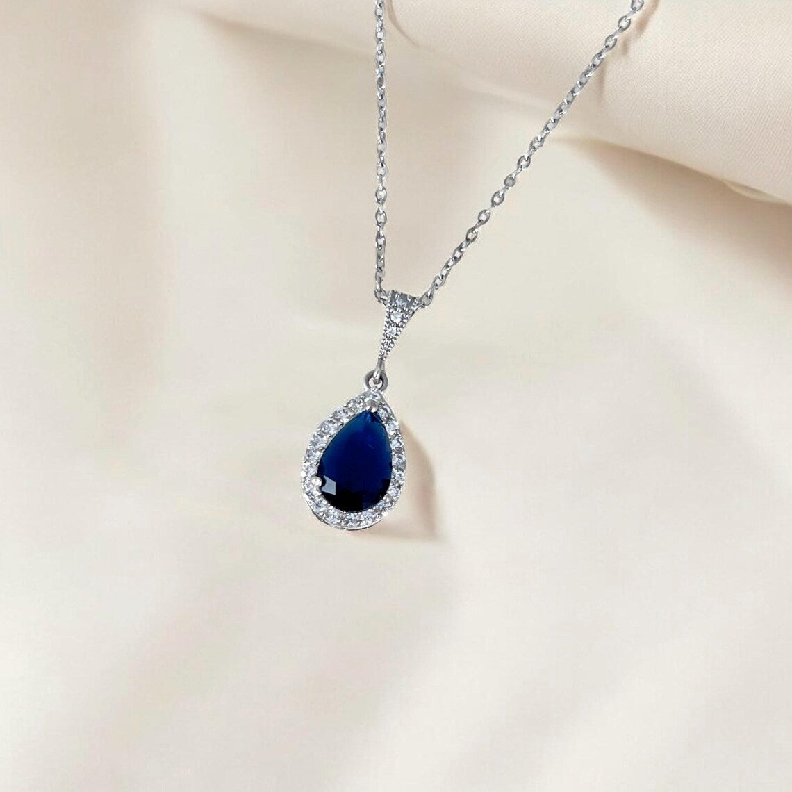 Teardrop-shaped blue gemstone necklace on a beige background