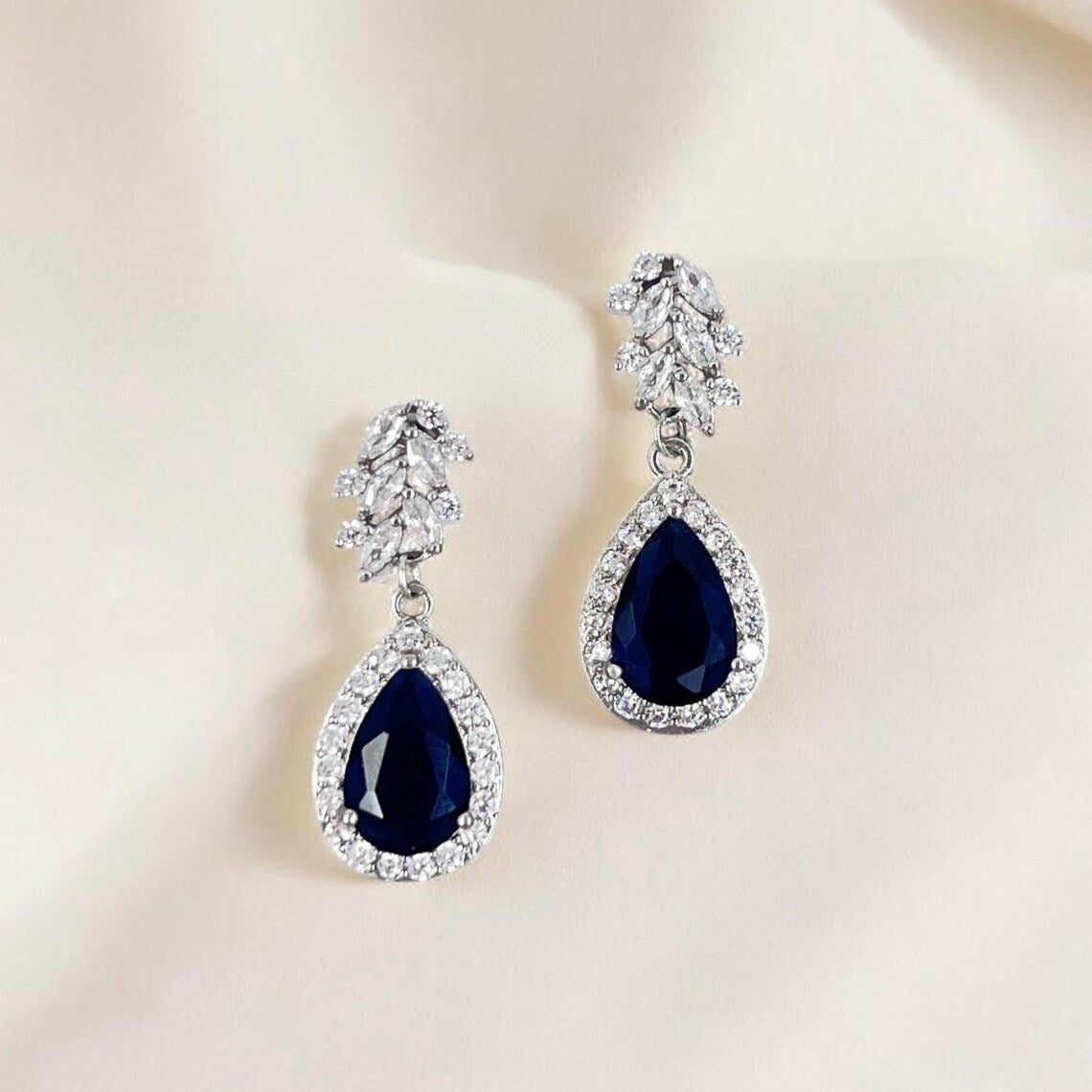 Pair of blue teardrop earrings with clear gemstones on a light background