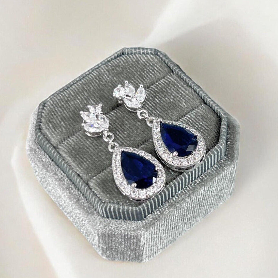 Teardrop-shaped blue gemstone earrings in a gray jewelry box on a white background