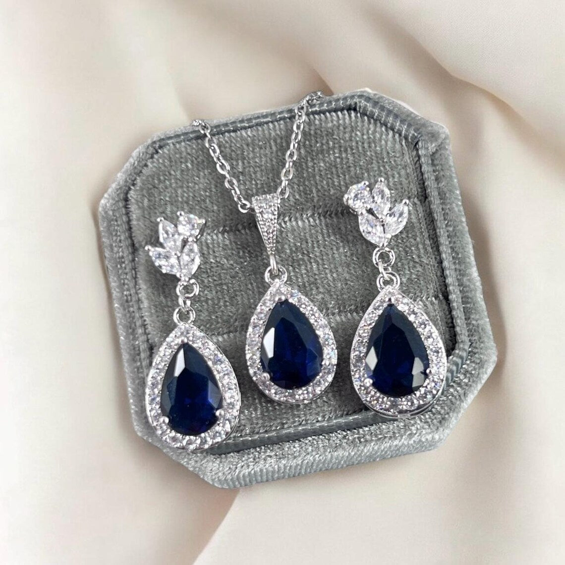 Jewelry set with blue teardrop stones in a gray velvet box on a light background