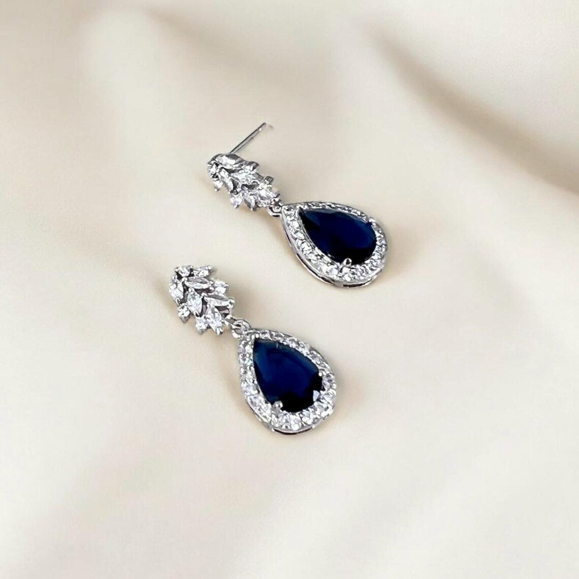 Pair of blue teardrop earrings with silver detailing on a beige background