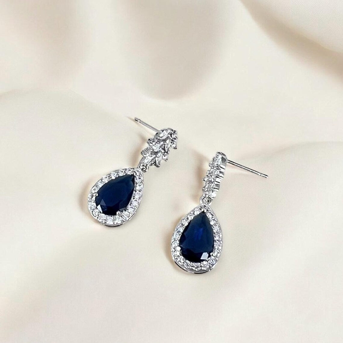 Pair of blue teardrop earrings with clear stones on a beige background