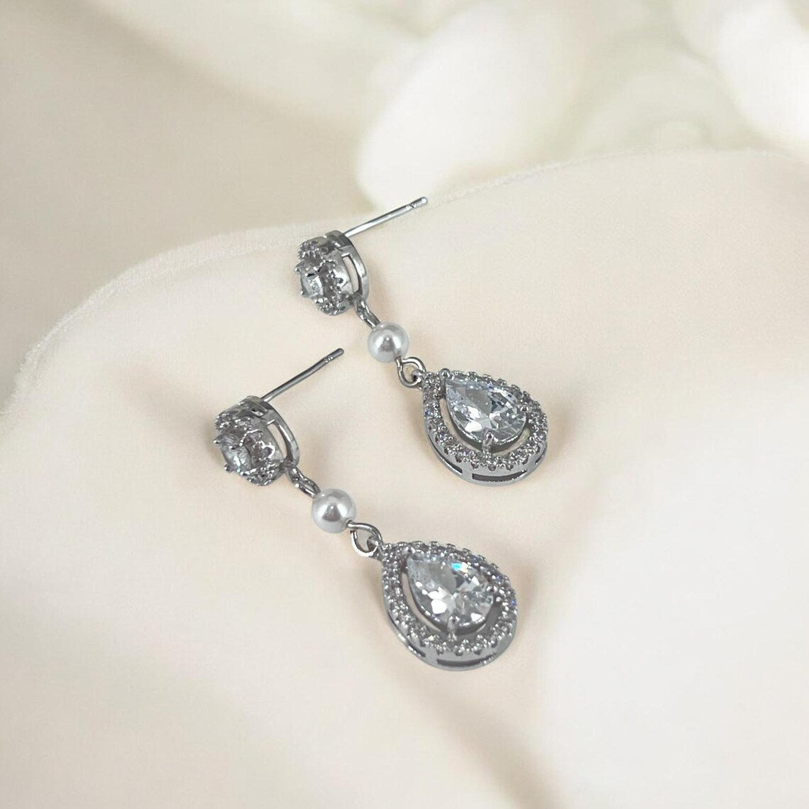 Close-up of teardrop crystal earrings highlighting halo setting and glossy pearl detail