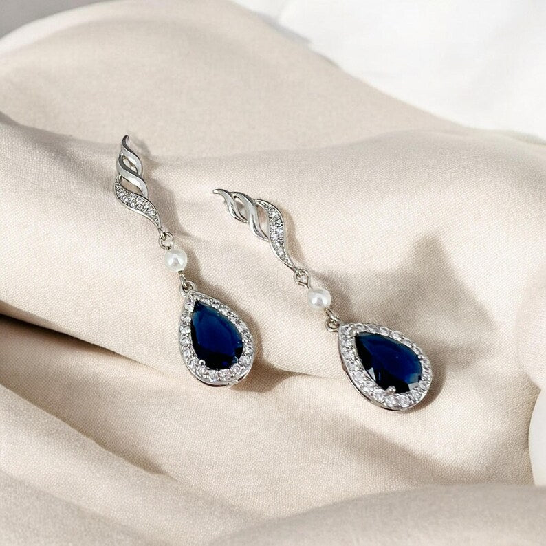 Pair of earrings with blue teardrop stones and pearl accents on a beige fabric background