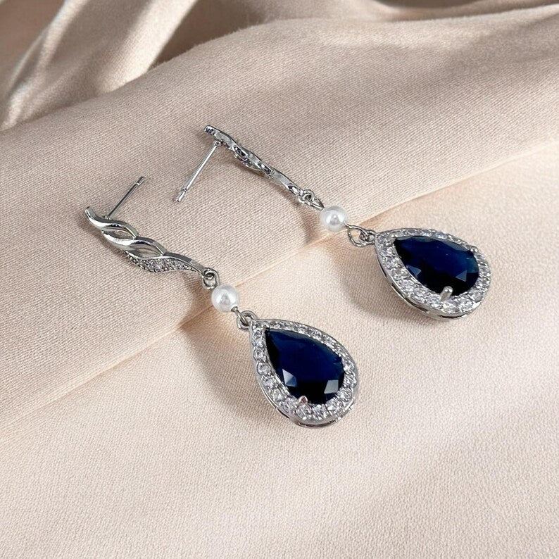 Pair of blue teardrop earrings with silver detailing on a beige fabric background