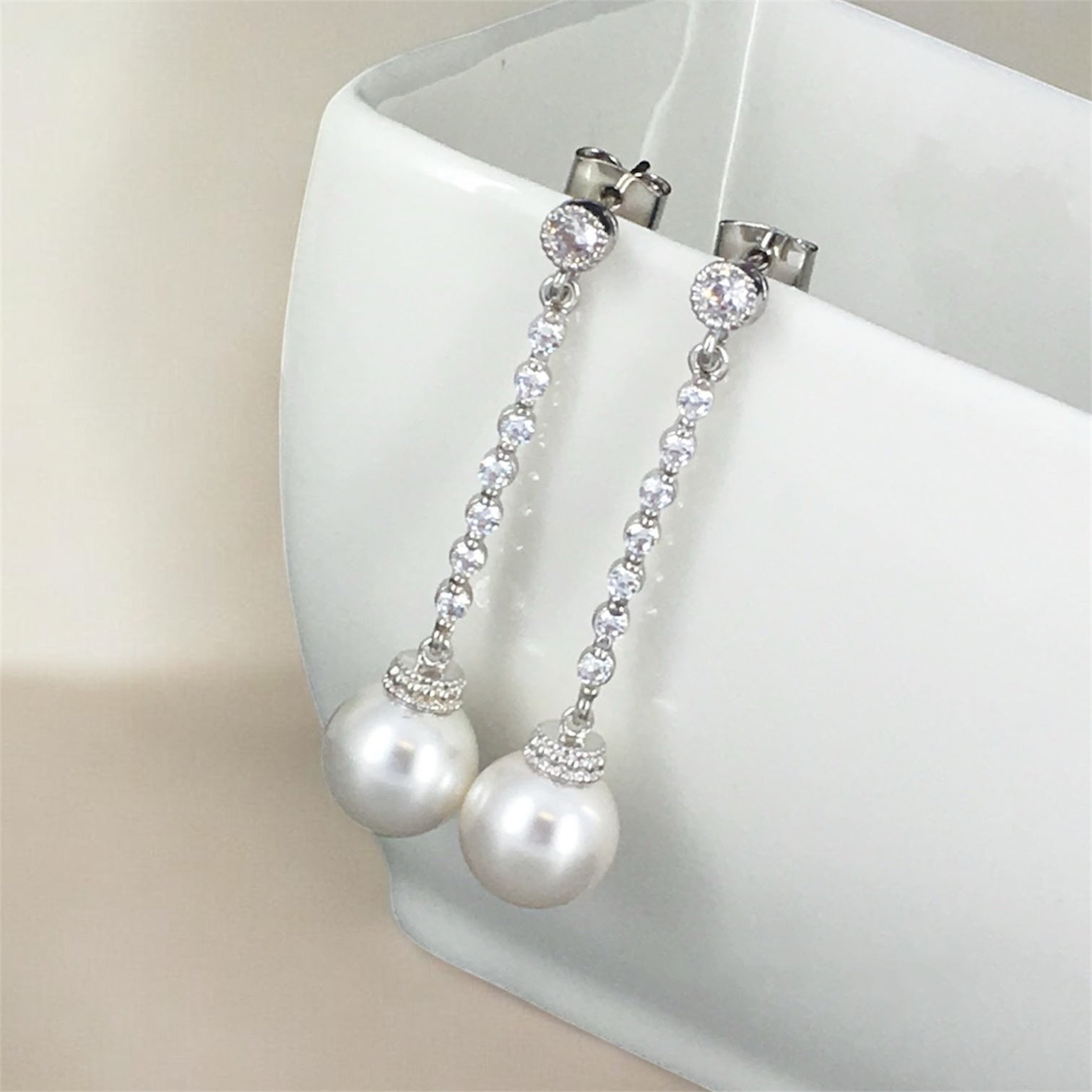 Long pearl crystal drop earrings photographed on white display with soft lighting for elegant bridal wedding jewelry inspiration